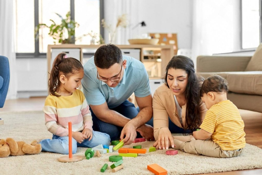 Family of four sitting on a rug at home in Dubai playing with colorful wooden building blocks